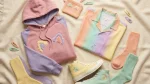 Flat-lay of pastel Eevee merch including a dusty pink hoodie, rainbow Hawaiian shirt and high-top sneakers