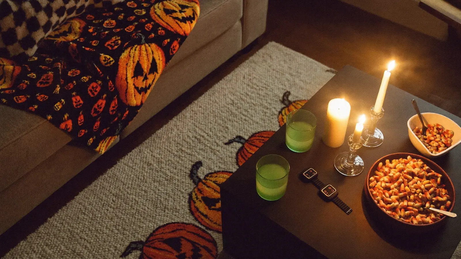 Living room set for a Halloween watch party with a pumpkin rug, throw blanket, candles and snacks