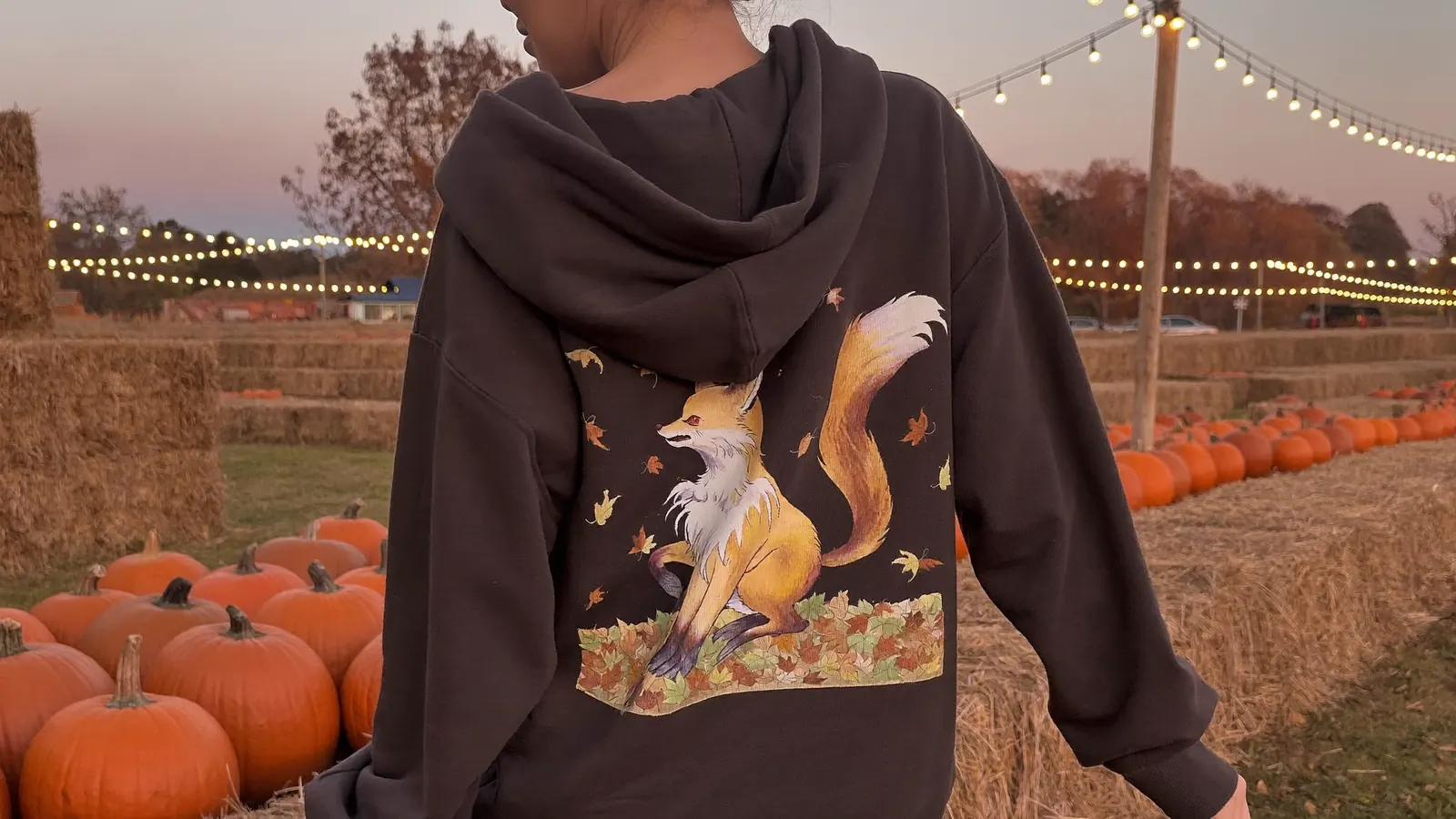 Woman at a pumpkin patch wearing an oversized anime hoodie with a fox illustration on the back