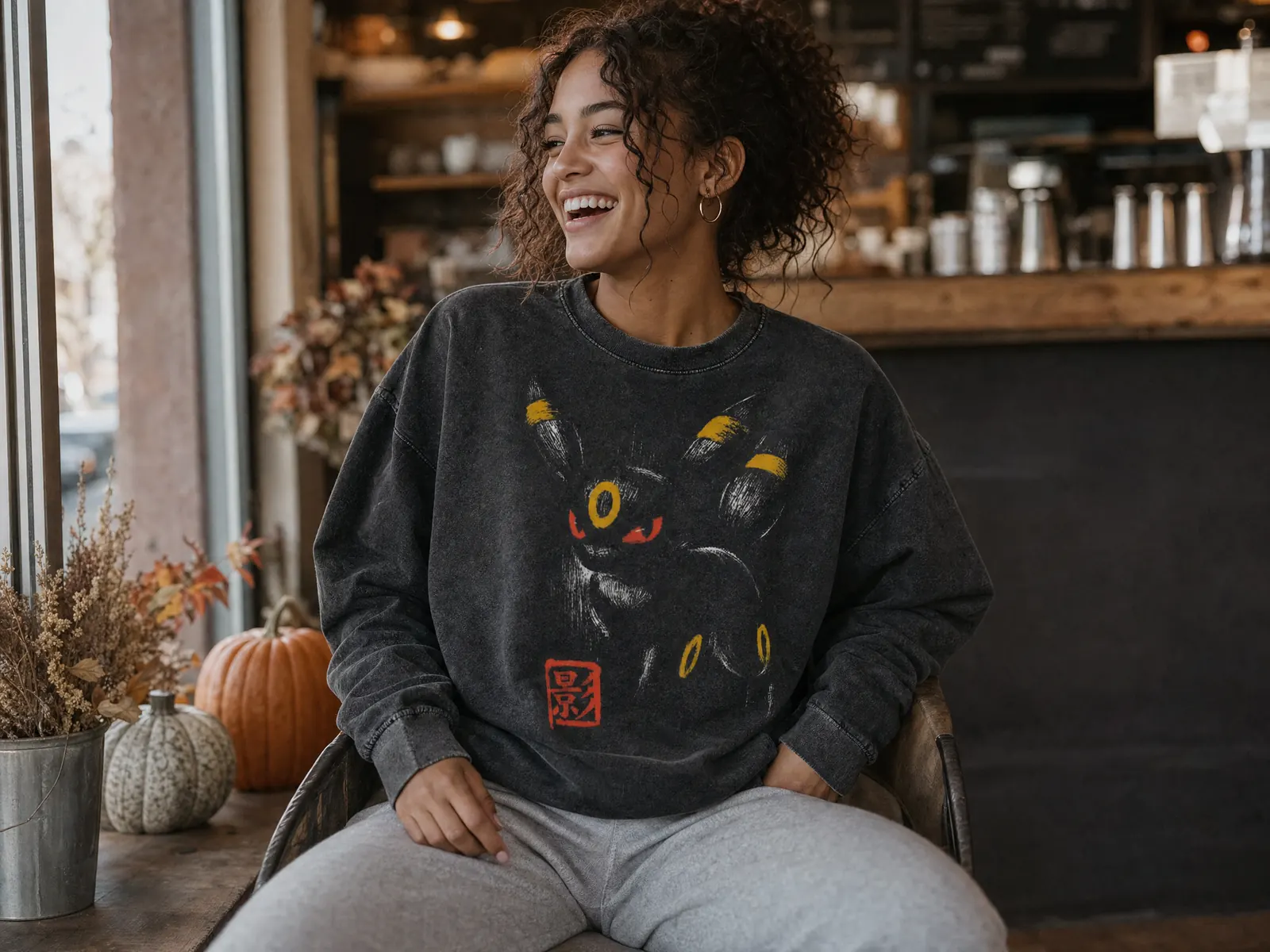 Laughing woman in a coffee shop wearing the vintage Umbreon Pokemon sweatshirt with grey joggers